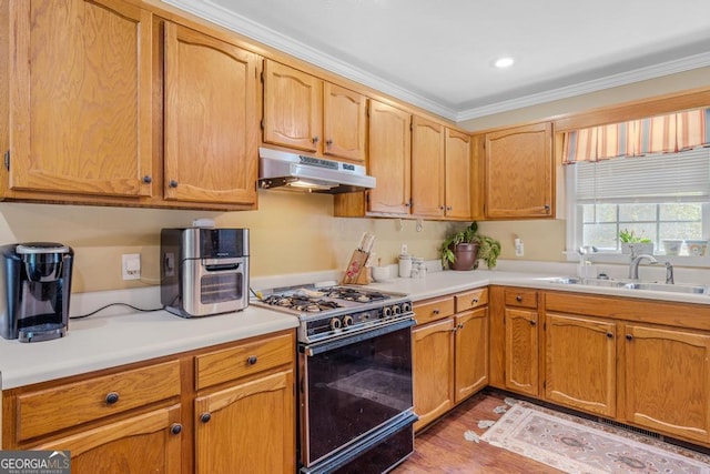 kitchen with light countertops, light wood-style flooring, gas stove, a sink, and under cabinet range hood