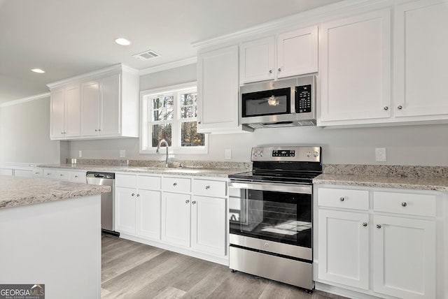 kitchen with a sink, white cabinetry, appliances with stainless steel finishes, light wood finished floors, and crown molding