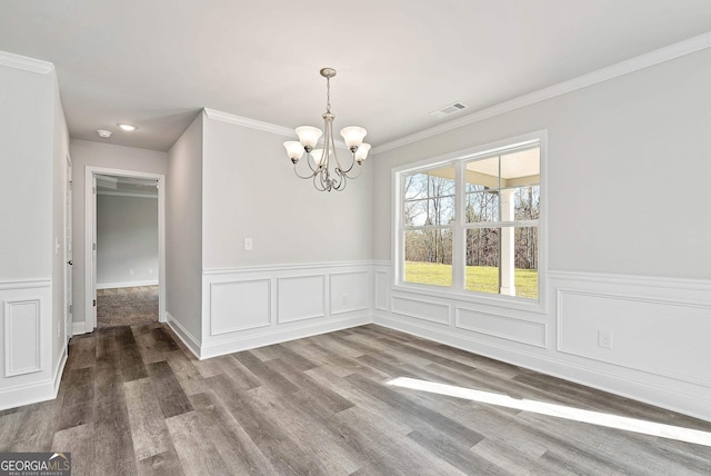 unfurnished dining area with visible vents, wainscoting, ornamental molding, wood finished floors, and a notable chandelier