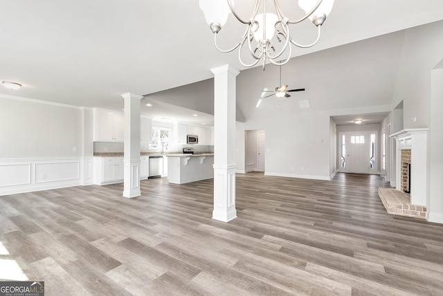 unfurnished living room featuring ornate columns, light wood-style flooring, a fireplace, and a ceiling fan