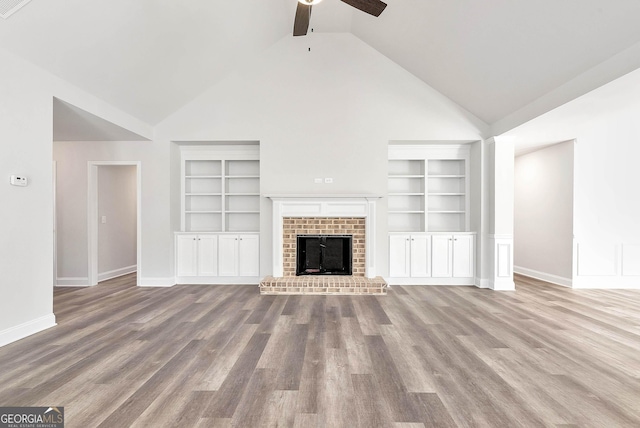 unfurnished living room with built in features, a fireplace, a ceiling fan, wood finished floors, and baseboards