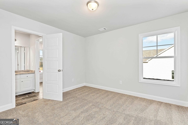 unfurnished bedroom with carpet, visible vents, ensuite bath, and baseboards