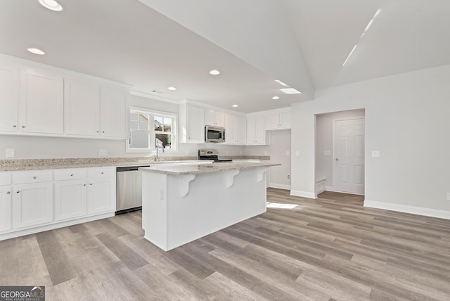 kitchen featuring light stone counters, a center island, appliances with stainless steel finishes, white cabinets, and light wood-type flooring