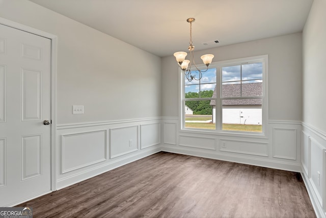 empty room featuring a wainscoted wall, dark wood finished floors, visible vents, and a notable chandelier