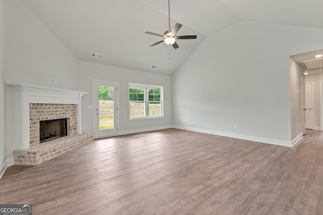 unfurnished living room with visible vents, attic access, a brick fireplace, ceiling fan, and wood finished floors