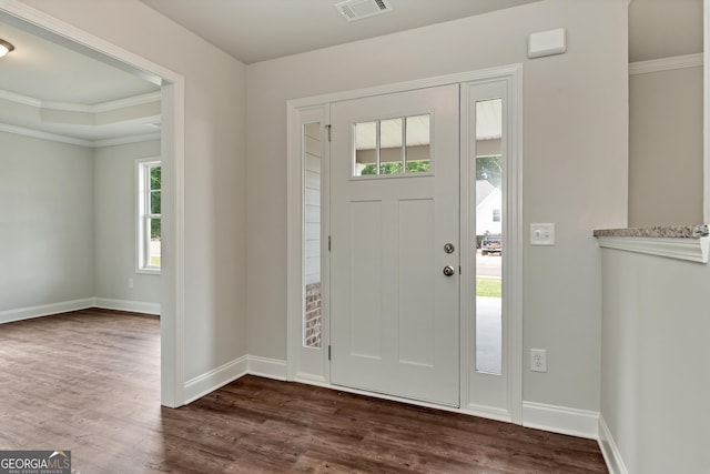 foyer entrance with ornamental molding, dark wood-style flooring, visible vents, and baseboards