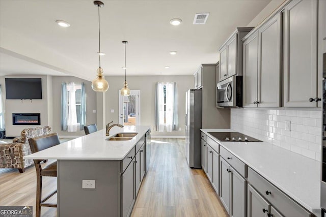 kitchen with a sink, visible vents, open floor plan, appliances with stainless steel finishes, and gray cabinets