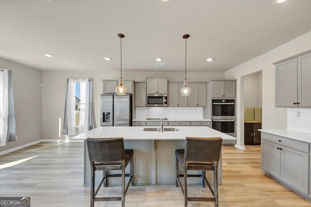 kitchen featuring gray cabinetry, stainless steel appliances, a sink, a kitchen breakfast bar, and light countertops