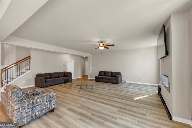 living room featuring ceiling fan, wood finished floors, baseboards, stairway, and a glass covered fireplace