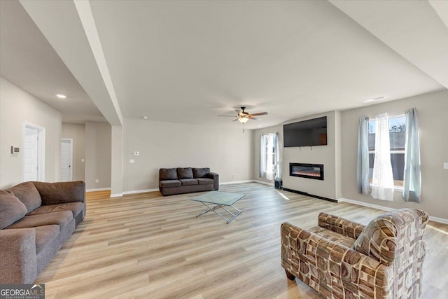 living room with a glass covered fireplace, light wood-style flooring, and baseboards