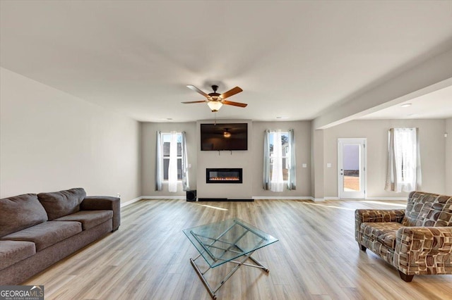 living room with light wood-style floors, baseboards, a wealth of natural light, and a glass covered fireplace