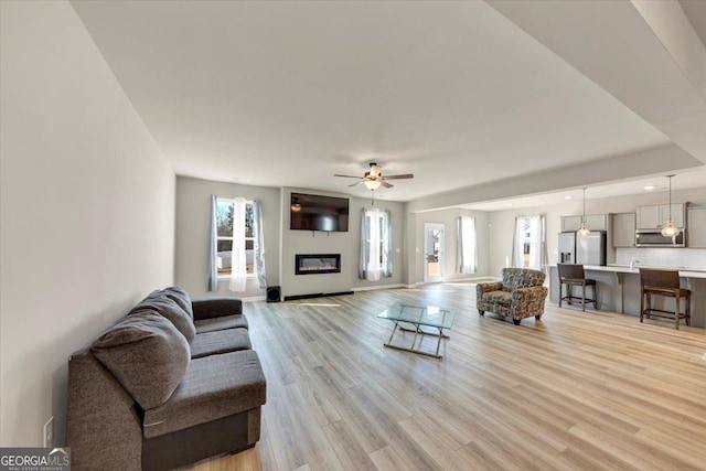 living room with ceiling fan, recessed lighting, baseboards, light wood-type flooring, and a glass covered fireplace