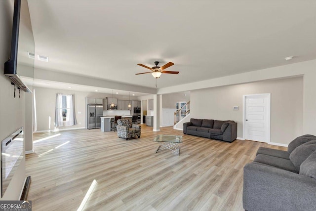 living room featuring light wood-style floors, ceiling fan, stairway, and baseboards