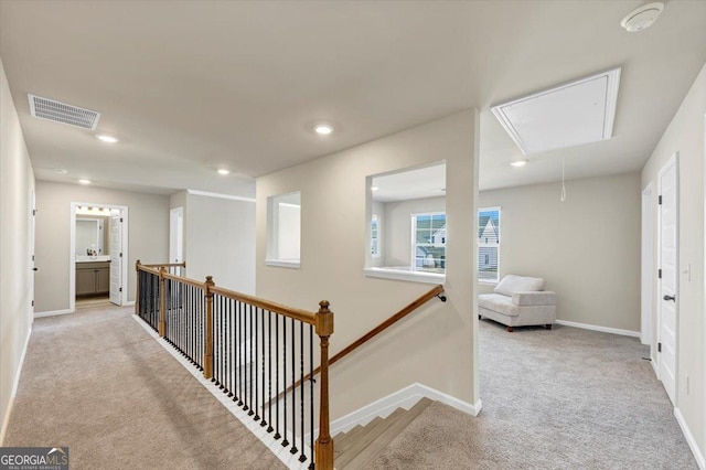 hallway with visible vents, an upstairs landing, carpet flooring, and attic access