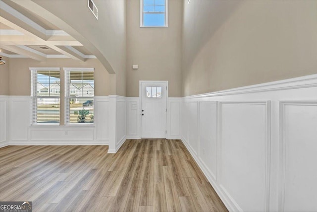 foyer featuring arched walkways, a wainscoted wall, coffered ceiling, beam ceiling, and light wood finished floors