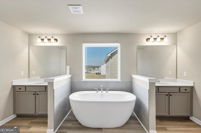 full bathroom with two vanities, visible vents, a freestanding bath, and wood finished floors