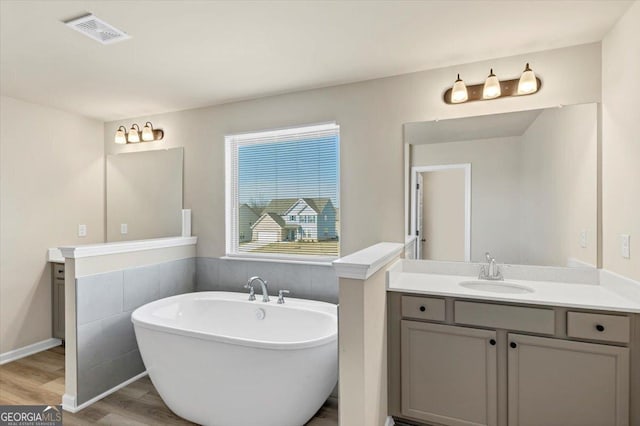 bathroom with visible vents, a freestanding bath, vanity, and wood finished floors