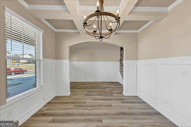 unfurnished dining area with arched walkways, coffered ceiling, beamed ceiling, light wood-type flooring, and a chandelier