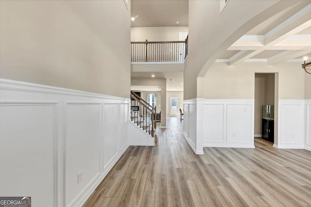 foyer entrance featuring a decorative wall, a wainscoted wall, light wood-style floors, stairway, and beamed ceiling