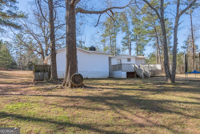 back of house with a trampoline, a deck, and a yard