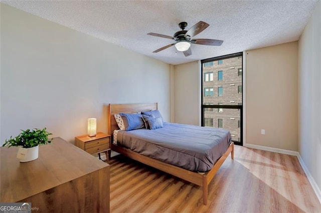 bedroom featuring light wood finished floors, expansive windows, ceiling fan, a textured ceiling, and baseboards