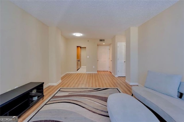 living room featuring light wood-type flooring, visible vents, baseboards, and a textured ceiling