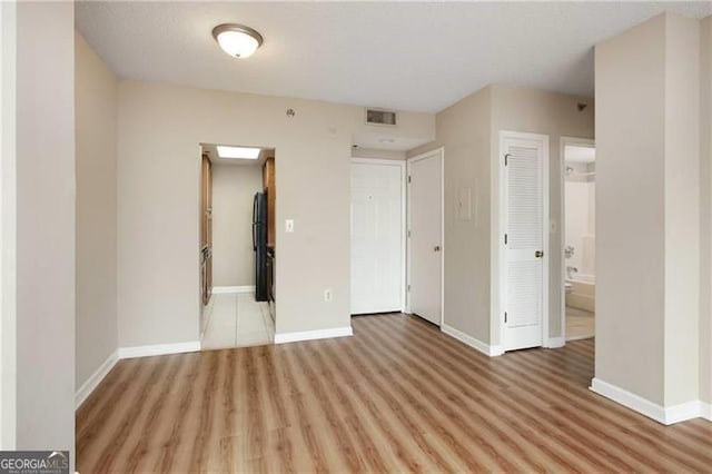 unfurnished bedroom with freestanding refrigerator, baseboards, visible vents, and light wood finished floors