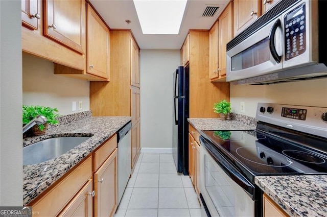 kitchen with a skylight, a sink, visible vents, appliances with stainless steel finishes, and light stone countertops