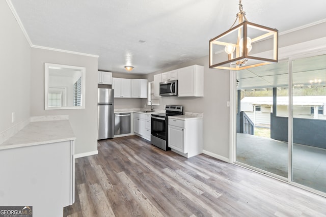 kitchen with appliances with stainless steel finishes, ornamental molding, wood finished floors, white cabinetry, and a sink