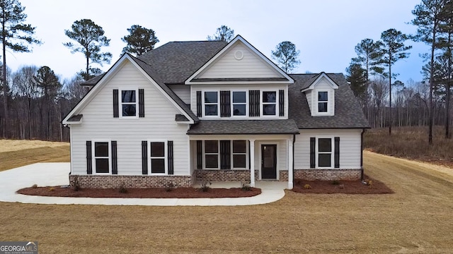 view of front of house featuring a shingled roof, a front lawn, and brick siding