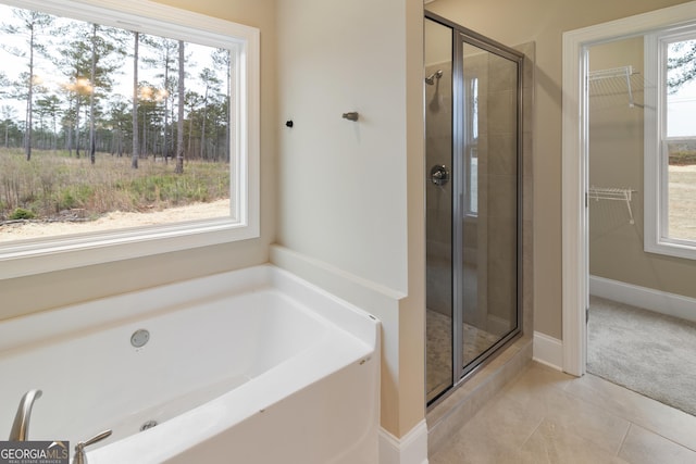 bathroom featuring baseboards, a bath, tile patterned floors, a stall shower, and a walk in closet