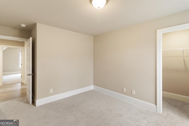 unfurnished bedroom with a walk in closet, a closet, light carpet, and baseboards