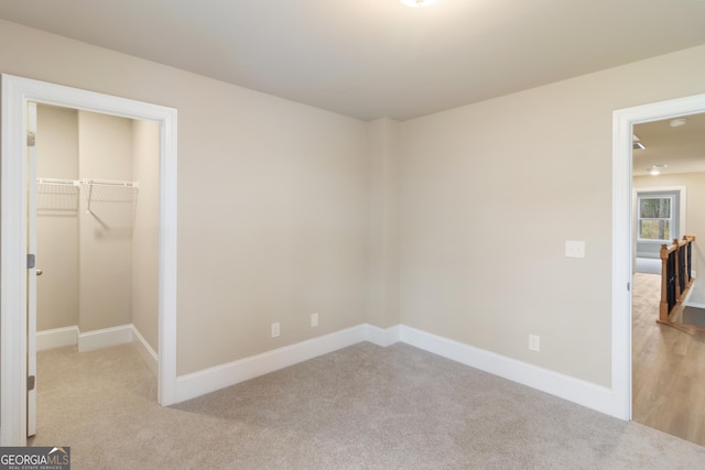 bedroom featuring light carpet, a closet, a walk in closet, and baseboards