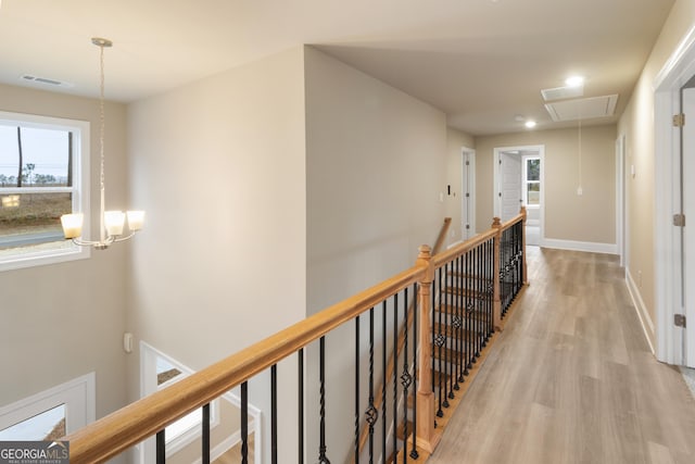 hallway with attic access, visible vents, baseboards, an upstairs landing, and light wood-type flooring