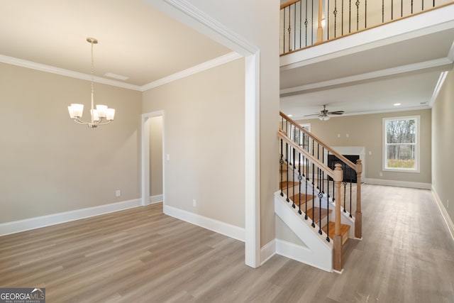 staircase featuring ceiling fan with notable chandelier, ornamental molding, wood finished floors, and baseboards