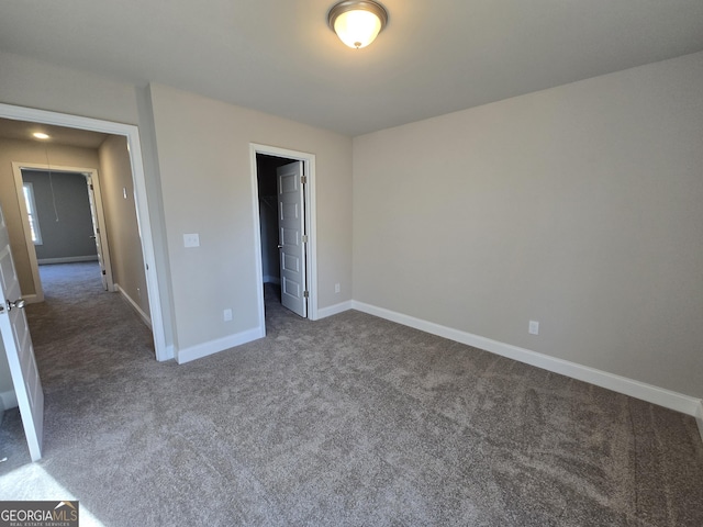 unfurnished bedroom featuring attic access, dark colored carpet, a walk in closet, and baseboards