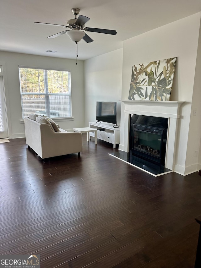 living area with wood finished floors, visible vents, baseboards, a ceiling fan, and a glass covered fireplace