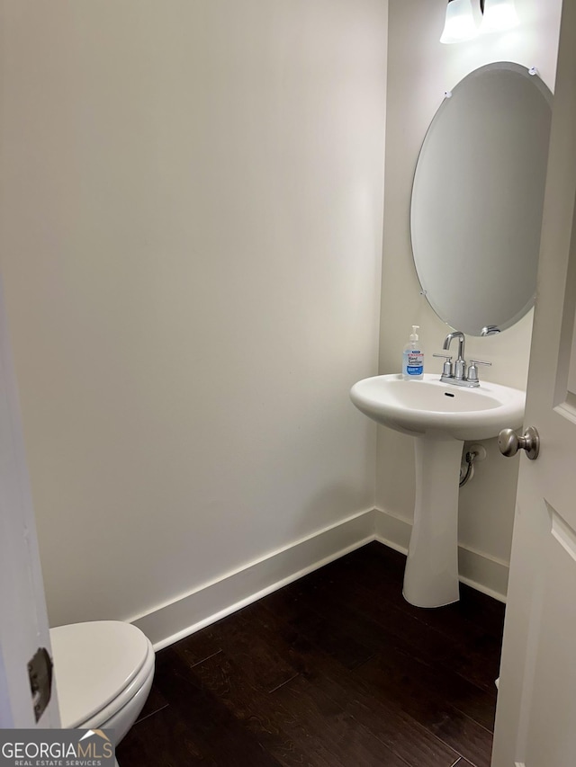 half bathroom with a sink, wood finished floors, toilet, and baseboards