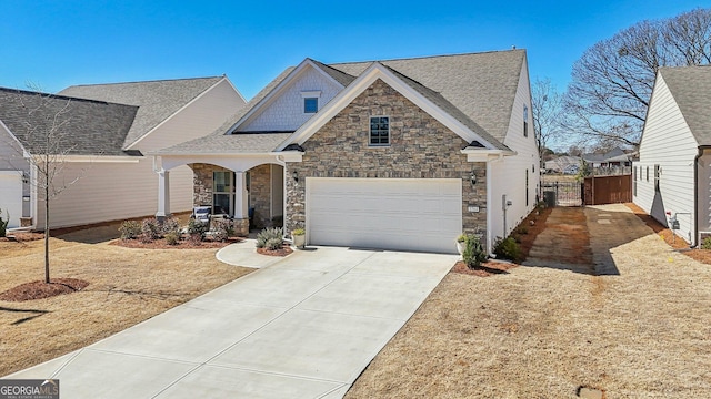 view of front of house with driveway, stone siding, an attached garage, a gate, and fence