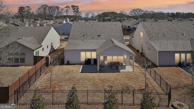 back of house at dusk with a patio area, a fenced backyard, and a residential view