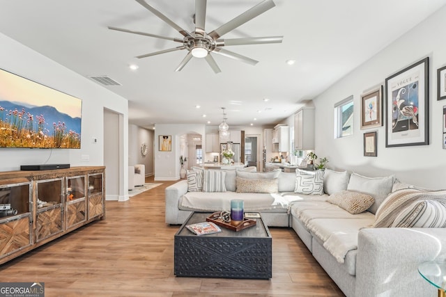 living room with visible vents, arched walkways, ceiling fan, light wood-style floors, and recessed lighting