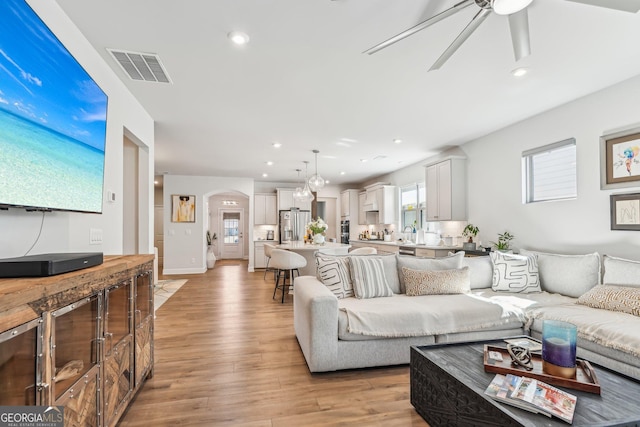 living area featuring visible vents, arched walkways, light wood-style flooring, and recessed lighting