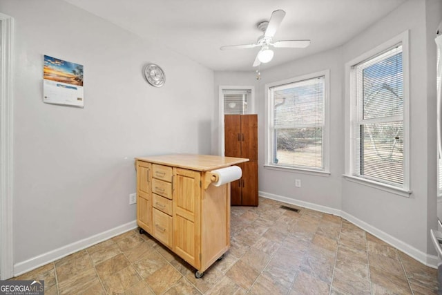 office area featuring baseboards, visible vents, ceiling fan, and stone finish flooring