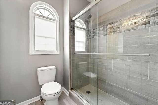 bathroom featuring a stall shower, baseboards, toilet, and wood finished floors