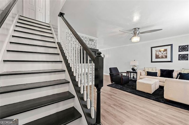 stairs featuring ceiling fan, ornamental molding, and wood finished floors