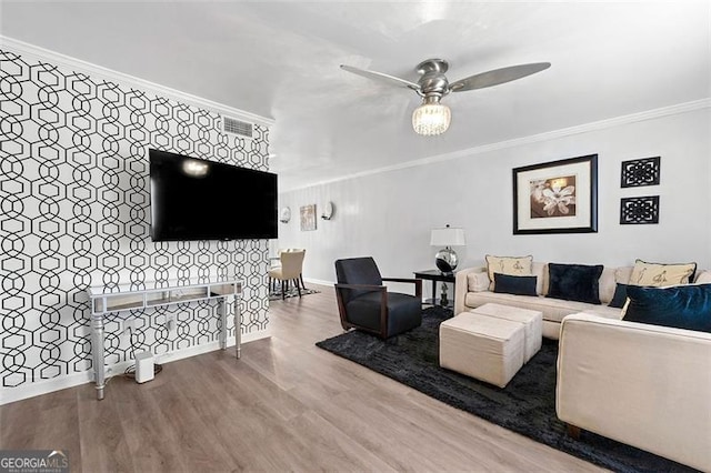 living area with crown molding, an accent wall, ceiling fan, wood finished floors, and baseboards