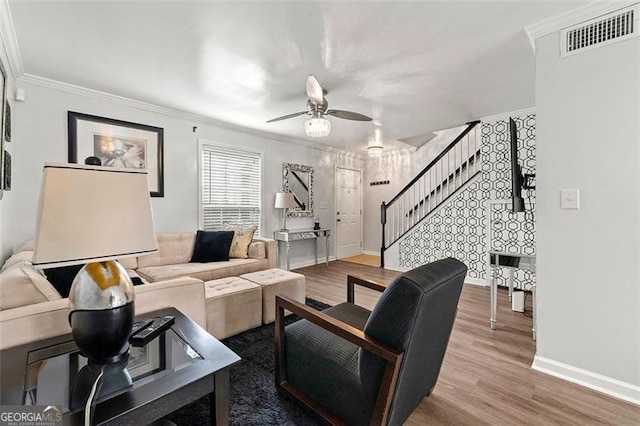 living area featuring crown molding, visible vents, wood finished floors, baseboards, and stairs