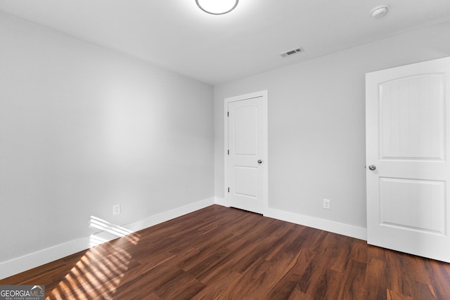 unfurnished room with baseboards, visible vents, and dark wood-type flooring