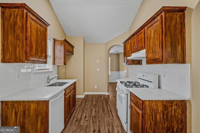 kitchen with white appliances, arched walkways, wood finished floors, under cabinet range hood, and a sink