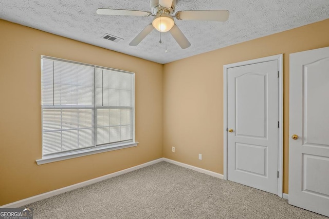 empty room featuring visible vents, a ceiling fan, carpet flooring, a textured ceiling, and baseboards